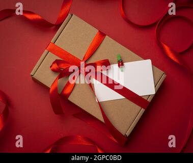 rectangular brown cardboard box tied with a silk red ribbon on a red background, top view, close up Stock Photo