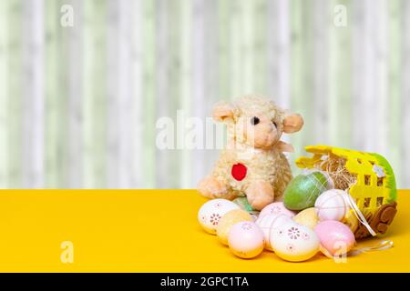 Easter greeting card template. Decorative composition of colorful eggs with a easter lamb and eggs on a yellow table in front of modern abstract curta Stock Photo