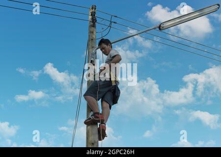 Electrician, repairman are climbing and work on electric pole. Concept of working wrong way and no safety no helmet. Stock Photo