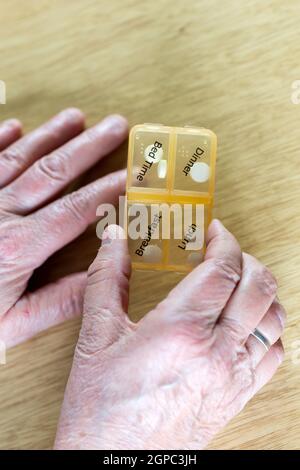 Closeup of an elderly senior woman's hands taking her medication for the week in a pill box on wooden table, business,health concept close up Stock Photo