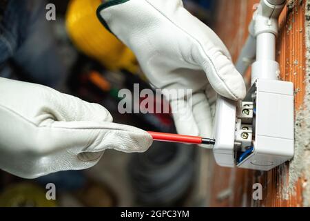 Top view. Electrician worker at work with screwdriver installs the switches of a residential electrical system. Working safely with protective gloves. Stock Photo