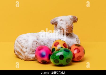 Easter card template. Close-up of a traditional easter lamb cake and some colorful eggs on yellow table and background. Copy space for design. Macro. Stock Photo