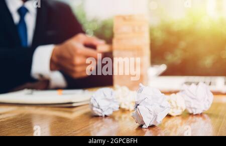 Business man risk he pulling block wood tower and have crumpled paper on desk table Stock Photo
