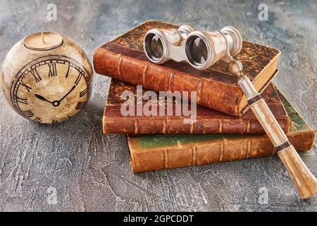 Still life with antique books, theatrical binoculars and candles in the shape of clock. Stock Photo