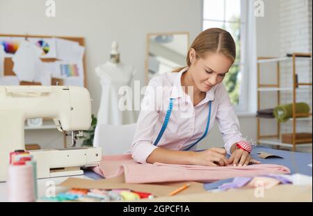 Young skillful seamstress woman adjusts fabric with pins while working in sewing workshop. Stock Photo