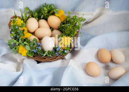 Beautiful spring bouquet in a wooden basket with Easter painted eggs, eggs with cute faces, eggs and feathers lie on the side. Easter colorful card. V Stock Photo