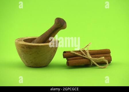 Cinnamon sticks bundle tied with jute string and wooden mortar with pestle on green background and free copy space for text Stock Photo