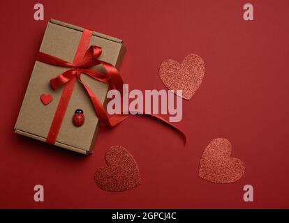 rectangular brown cardboard box tied with a silk red ribbon on a red background, top view, close up Stock Photo