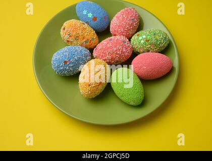 decorative easter eggs in a round white ceramic plate on a yellow background, top view Stock Photo