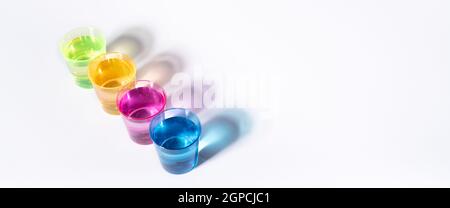 Plastic multi-colored glasses with liquid on a white background with highlights. Layout, mockup. Stock Photo