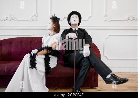 Two mime artists, lady and gentleman sitting on sofa. Pantomime theater, parody comedian, positive emotion, humour performance, funny face mimic and g Stock Photo