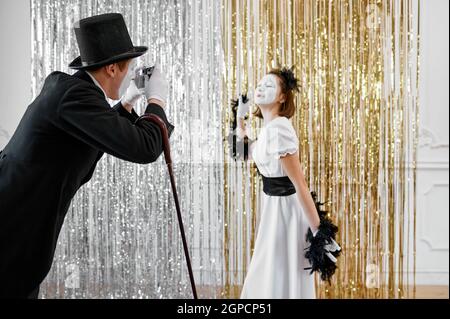 Two mime artists, lady poses at gentleman with camera. Pantomime theater, parody comedian, positive emotion, humour performance, funny face mimic and Stock Photo