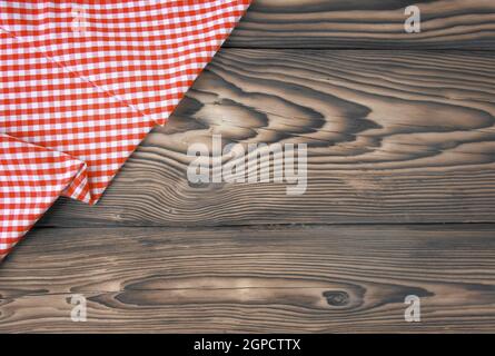 Empty table background. Top view of a empty red and white checkered kitchen cloth, textile, tablecloth or napkin on a rustic brown table. Template for Stock Photo