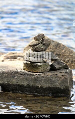 A cairn stack on a large flat rock near water. Stock Photo