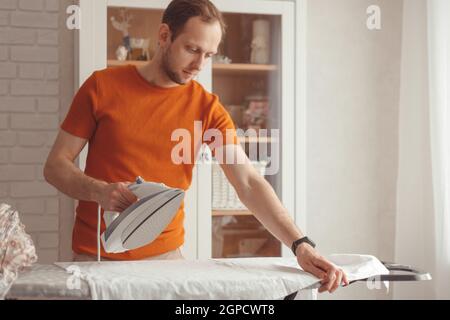 Young caucasian man ironing children's sheet on ironing board at home. Men doing home chores Stock Photo