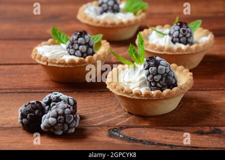 Homemade tartlets with blackberry, whipped cream and mint. Tasty sweet dessert concept Stock Photo