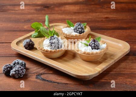 Homemade tartlets with blackberry, whipped cream and mint. Tasty sweet dessert concept Stock Photo