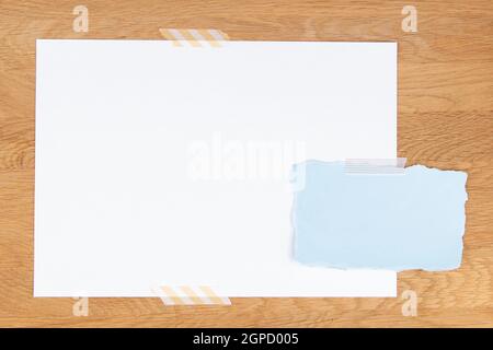 Blank white paper page and torn piece of blue paper attached with adhesive tape on wooden background Stock Photo