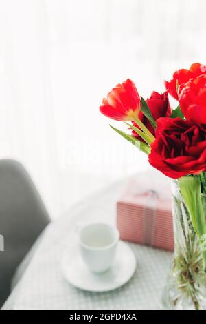 Red tulips bouquete on table, white coffee cup. Concept for greeting card for mothers day, international womans day or valentines day concept, birthda Stock Photo
