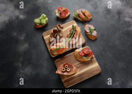 Brushetta or traditional Spanish tapas. Appetizers with Italian antipasti snacks. Variety of small sandwiches with prosciutto, cherry tomatoes, salmon Stock Photo