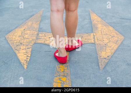 Girl wear red shoes  walking towards with yellow traffic arrow signage on an asphalt road background Stock Photo