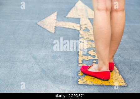 Girl wear red shoes  walking towards with yellow traffic arrow signage on an asphalt road background Stock Photo