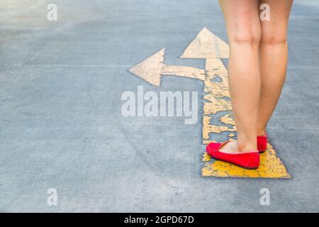 Girl wear red shoes  walking towards with yellow traffic arrow signage on an asphalt road background Stock Photo