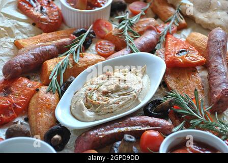 Grilled sausages and vegetables platter served with humus and pita bread, grilled mushrooms, cherry tomatoes, sweet potatoes and herbs. Barbecue grill Stock Photo