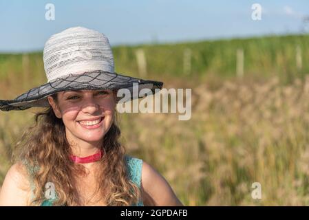 Blonde woman wearing a hat in a farm area and in the background a soy plantation. Portrait of a beautiful Brazilian girl outdoors. Rural lifestyle and Stock Photo