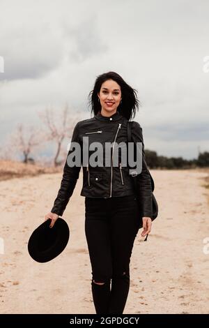 Brunette woman with leather jacket walking on a path with flowered almond trees Stock Photo