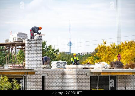 Vilnius, Lithuania - September 28 2021: New buildings or houses under construction with workers at work against cloudy sky with Vilnius TV tower Stock Photo