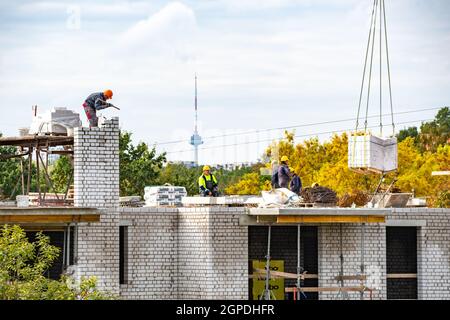 Vilnius, Lithuania - September 28 2021: New buildings or houses under construction with workers at work against cloudy sky with Vilnius TV tower Stock Photo