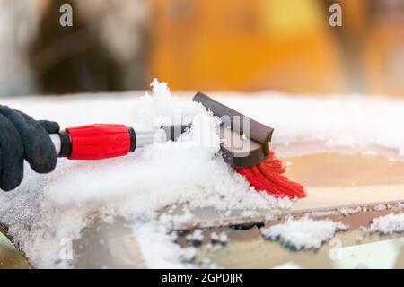 Human cleaning snowy cover from roof of the car in sunlight. Person sweeping snow from automobile with broom. Hand using a tool in winter. Stock Photo