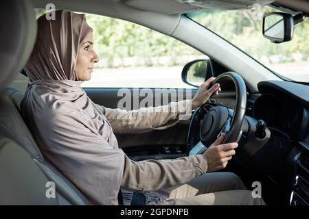 Horizontal side view portrait shot of beautiful confident Muslim woman going to somewhere by car Stock Photo