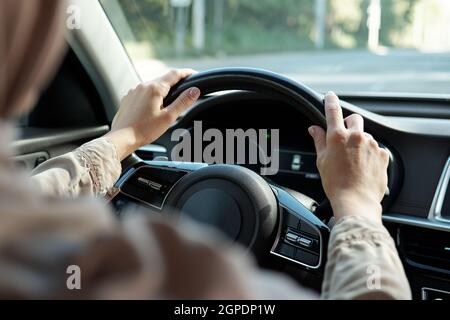 Horizontal over-the-shoulder rear view shot of unrecognizable Muslim woman wearing hijab driving her car Stock Photo