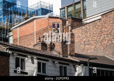Old chimney stacks and pots on top of traditional ancient houses and buildings in modern city with construction of new skyscrapers in the background. Stock Photo