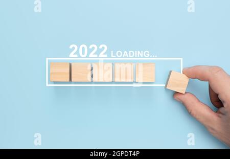 Loading new year 2022 with hand putting wood cube in progress bar. Loading new year 2022. Merry Christmas and happy new year business concept Stock Photo