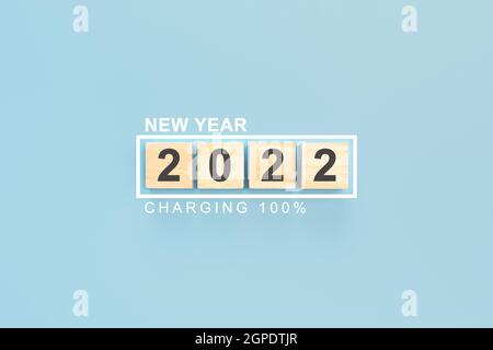 2022 on wooden cubes New Year Background. Year 2022 written on wooden cubes. 2022 new year wooden cubes on blue table background with status bar charg Stock Photo