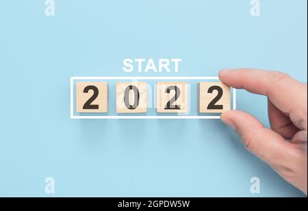 Start 2022 concept. Loading new year 2022 with hand putting wood cube in progress bar. Happy new year 2022. blue background Stock Photo