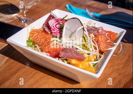 Salad of seafood on table. Sliced raw salmon, tuna, soy sprout with avocado sauce at restaurant. Stock Photo