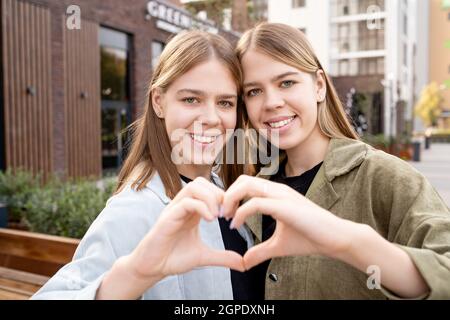 Happy affectionate twin girls in casualwear making shape of heart with hands Stock Photo