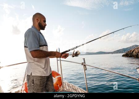 A guy fishing in the sea standing on a rock at the shore Stock Photo - Alamy