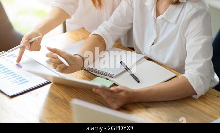 Two female executives are working in the office, discussing data on paperwork and a digital tablet. Stock Photo
