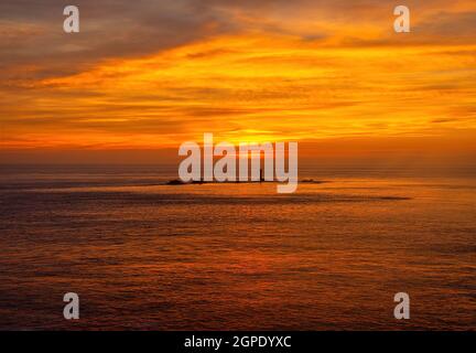 A beautiful sunset taken at Lands End as the sun sinks behind clouds into the sea. Longships Lighthouse is in silhouette. Stock Photo