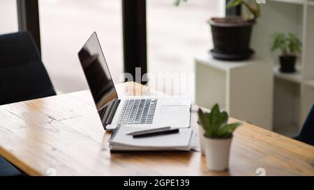 Side view of Opened portable laptop stand on wooden table with notebooks and decor in modern and cozy office Stock Photo