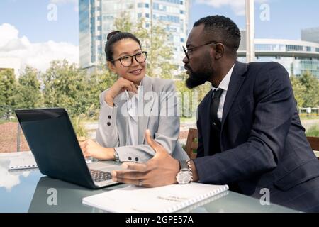 Two business partners discussing new strategies and ideas in front of laptop in outdoor cafe Stock Photo