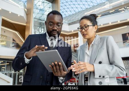 Two young intercultural colleagues preparing presentation inside large business center Stock Photo
