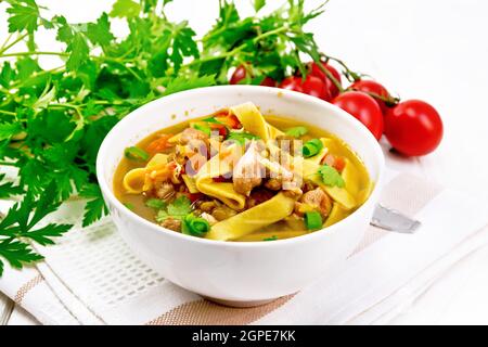 Soup with meat, tomatoes, vegetables, mung bean lentils and noodles in a bowl on a towel, parsley and spoon on wooden board background Stock Photo