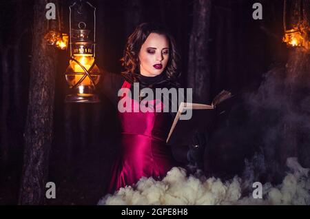 girl alone at night in the forest brews a potion and wonders for marriage, surrounded by candles and smoke Stock Photo