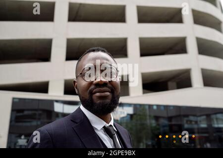 Young African banker in eyeglasses and formalwear standing in urban environment Stock Photo